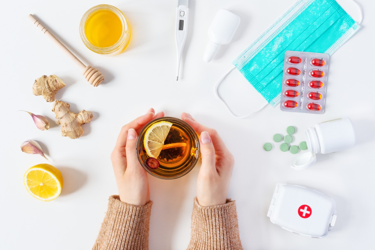 Composition of cold and flu treatments. Woman hands holding hot tea and different treatments around it. Medicaments and herbal medicine concept. Health care therapy. Flat lay, top view.